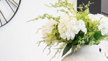 Een eettafel met een witte vaas vol witte bloemen en groen, blauwe borden en wijnglazen.