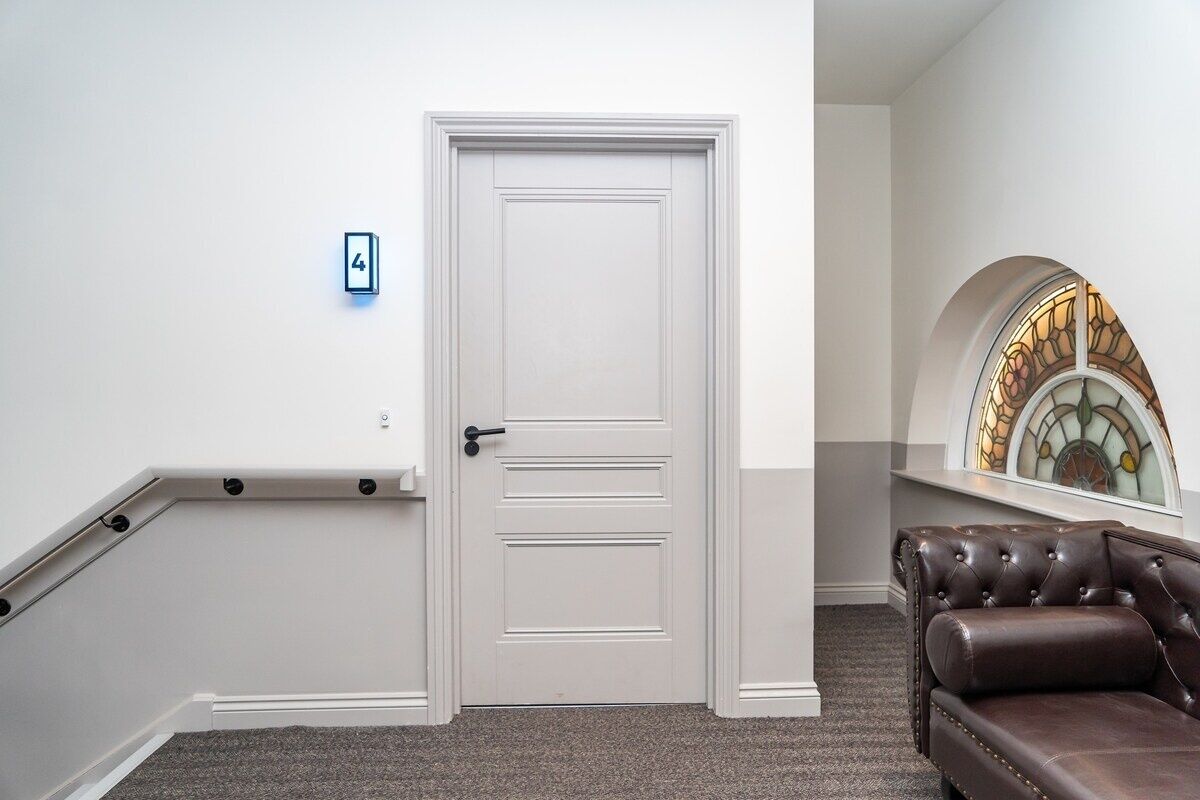 A hallway with a white door, a small blue sign, a brown leather couch, and a stained glass window.
