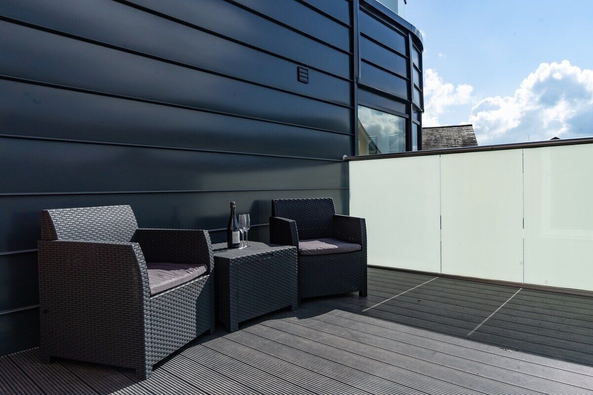 Terraza en la azotea con mobiliario de mimbre y una mesa, con un edificio moderno al fondo.
