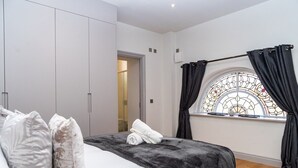 A bedroom with a bed, a wardrobe, a window with curtains, and a door leading to another room. - The Old Glassworks by Bevolve - Free Parking (Shrewsbury)