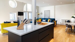 A modern kitchen with a central island, a dining area with chairs, a sofa, and a TV. - The Old Glassworks by Bevolve - Free Parking (Shrewsbury)
