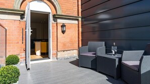 An outdoor seating area with wicker furniture and a table, a door leading to an interior space, and a small potted plant. - The Old Glassworks by Bevolve - Free Parking (Shrewsbury)