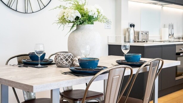 A modern dining area with a marble table, blue dinnerware, and a vase of white flowers. - The Old Glassworks by Bevolve - Free Parking (Shrewsbury)