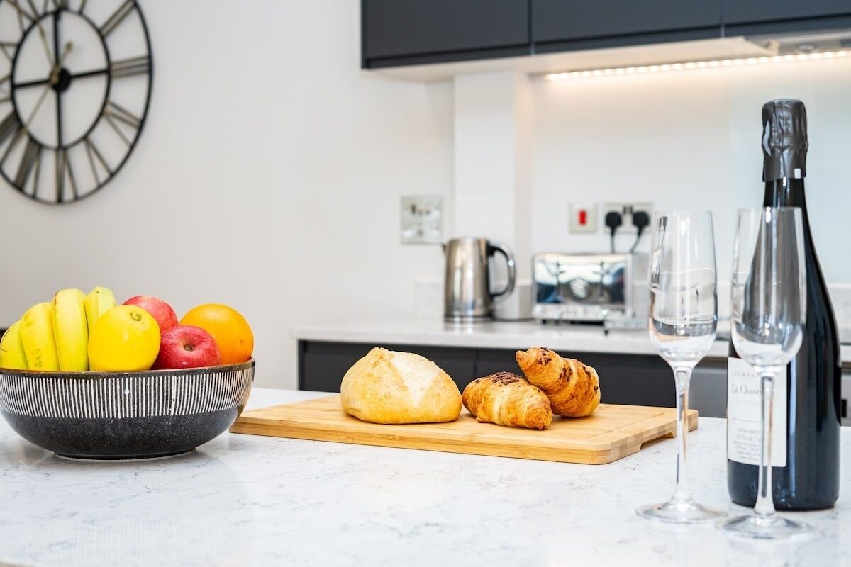 A kitchen counter with a bowl of fruit, croissants, and a wine bottle.