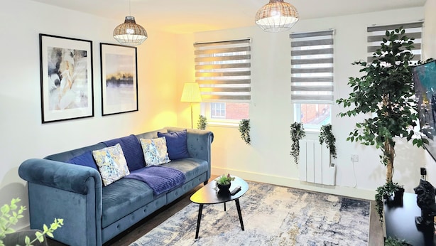 Ein Wohnzimmer mit einem blauen Sofa, zwei Wandlampen, einer Stehlampe und einem großen Fenster mit Jalousien.