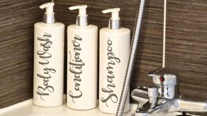 Drei weiße Flaschen mit den Aufschriften 'Baby Wash', 'Conditioner' und 'Shampoo' auf einem Badezimmerwaschbecken.