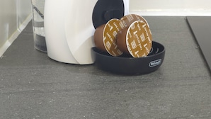 Eine Kaffeemaschine mit einer Tasse Wasser und zwei Kaffeekapseln auf einer Arbeitsplatte.