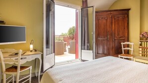 A bedroom with a bed, a desk, a chair, a wardrobe, and a balcony with wicker furniture. - Logis Hôtel Le Coq Hardi (Pouilly-sur-Loire)