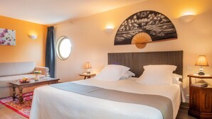 A hotel room with a bed, a sofa, a round window, and a wall-mounted artwork. - Logis Hôtel Le Coq Hardi (Pouilly-sur-Loire)