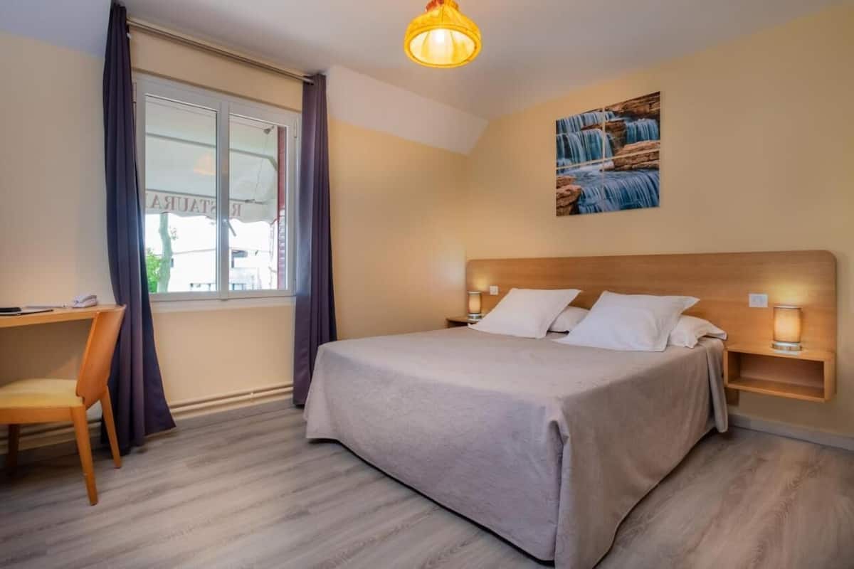 A bedroom with a bed, bedside lamps, a desk, and a window with curtains.