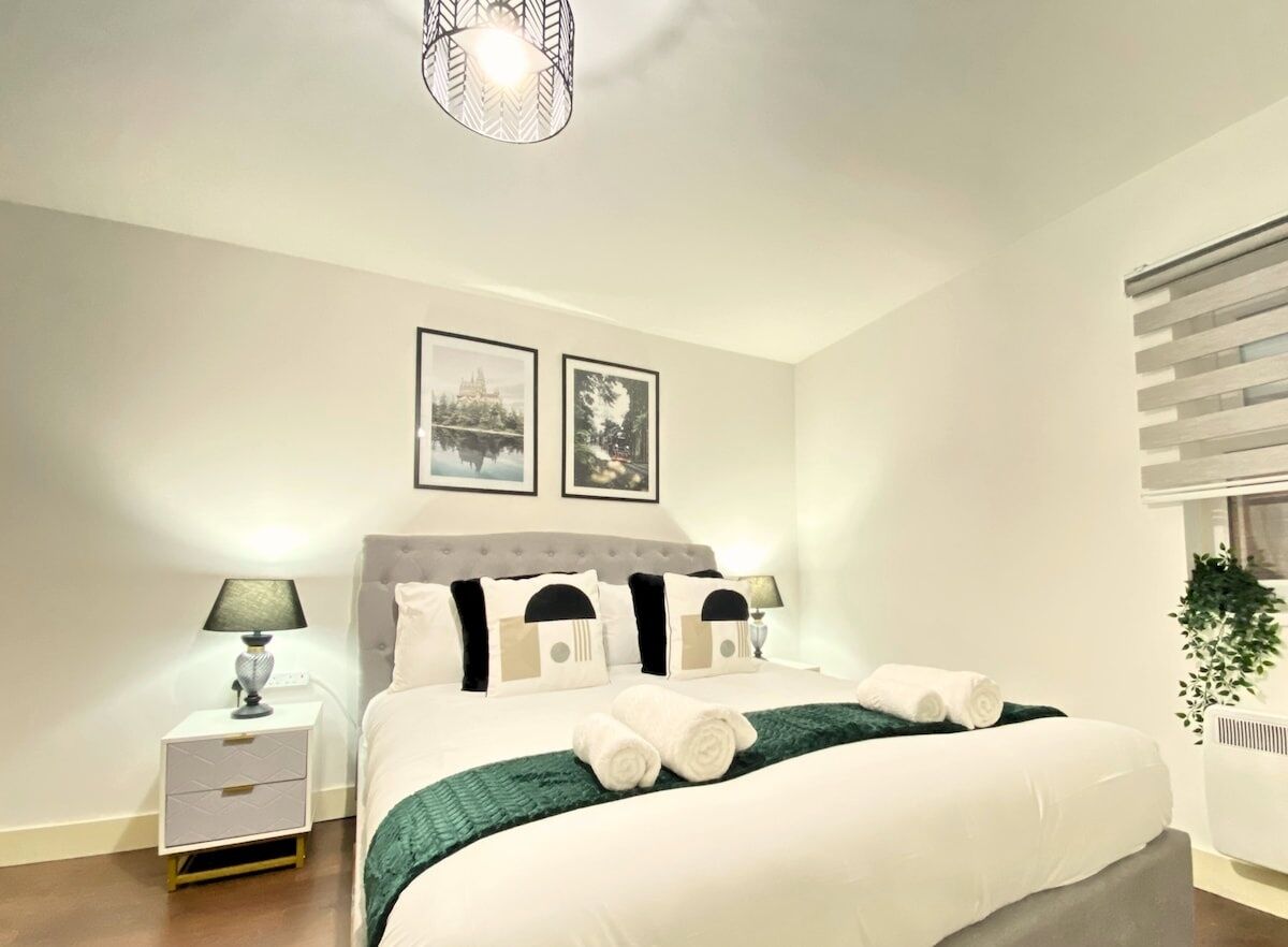 Un dormitorio ordenado con cama, lámparas de noche, mesita de noche y dos cuadros en la pared.