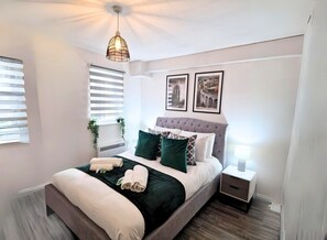 Een keurig opgemaakt slaapkamer met een bed, nachtkastjes en een hanglamp.