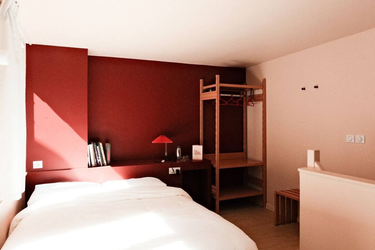A bedroom with a bunk bed, a bedside table with a lamp, a small shelf with books, and a closet with a hanging rack.