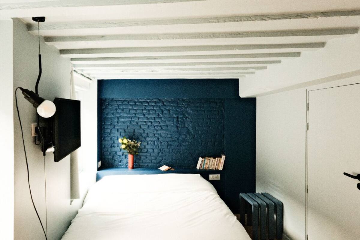 A bedroom with a white bed, a blue textured wall, a small potted plant, and a bookshelf.