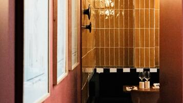 Un estrecho pasillo con pared de baldosas, una obra de arte enmarcada a la izquierda y una pequeña zona de estar con mesa y sillas al final.