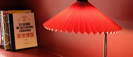 A red folding table lamp with a black base, placed on a red surface with a book titled "Le guide de la cuisine" beside it.