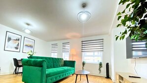 Una sala de estar moderna con un sofá verde, piso de madera, una mesa de centro redonda y un televisor sobre un mueble de madera.