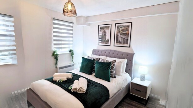 Un dormitorio ordenado con cama, mesitas de noche y una lámpara colgante.