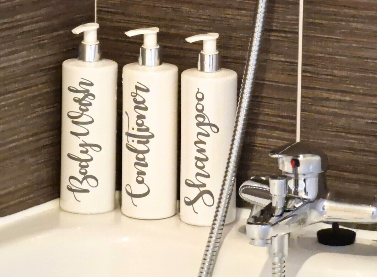 Drie witte flessen met de tekst 'Baby Wash', 'Conditioner' en 'Shampoo' op een wastafel in een badkamer.