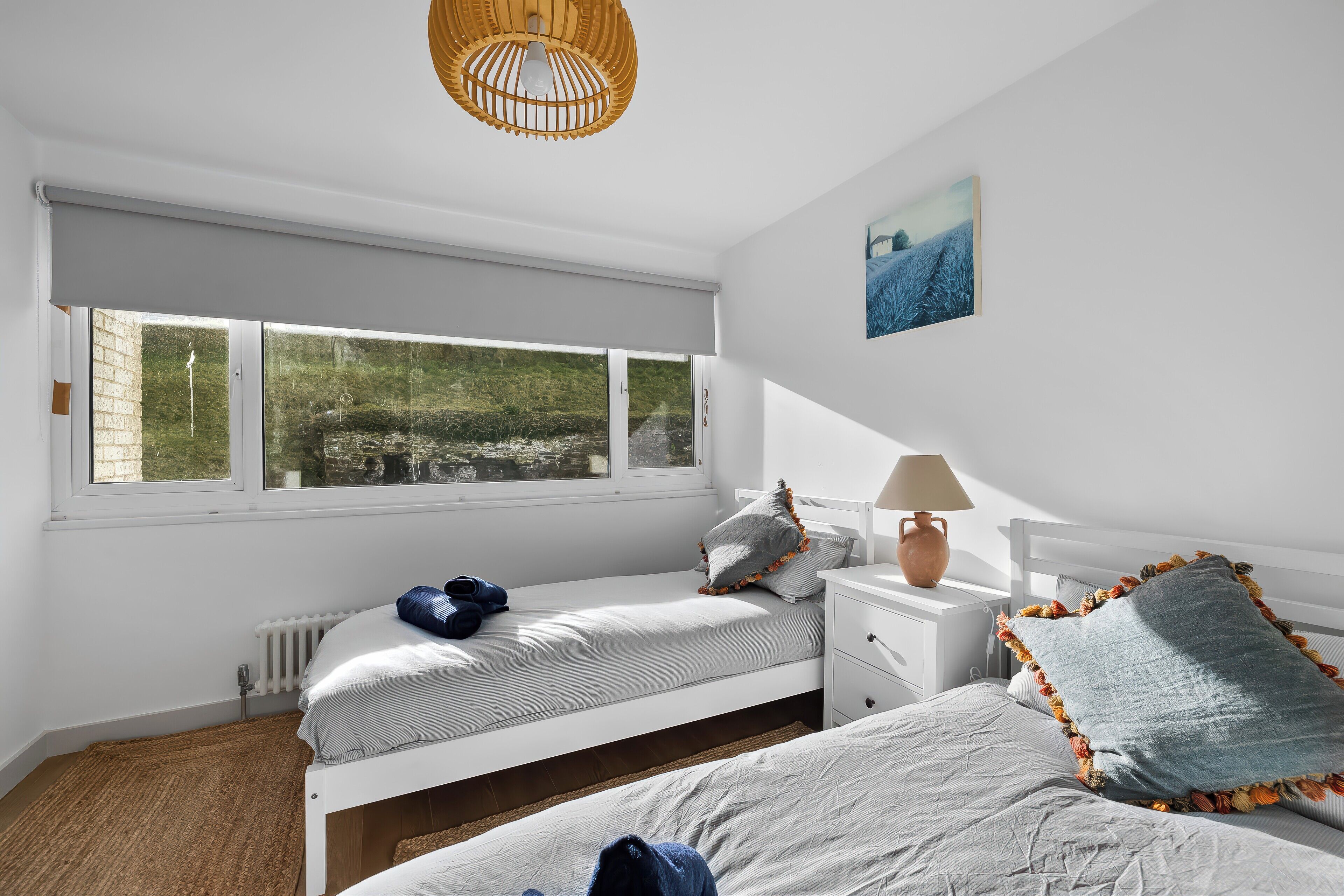 Ein Schlafzimmer mit großem Fenster, einem Bett, einem Nachttisch und einer Lampe.