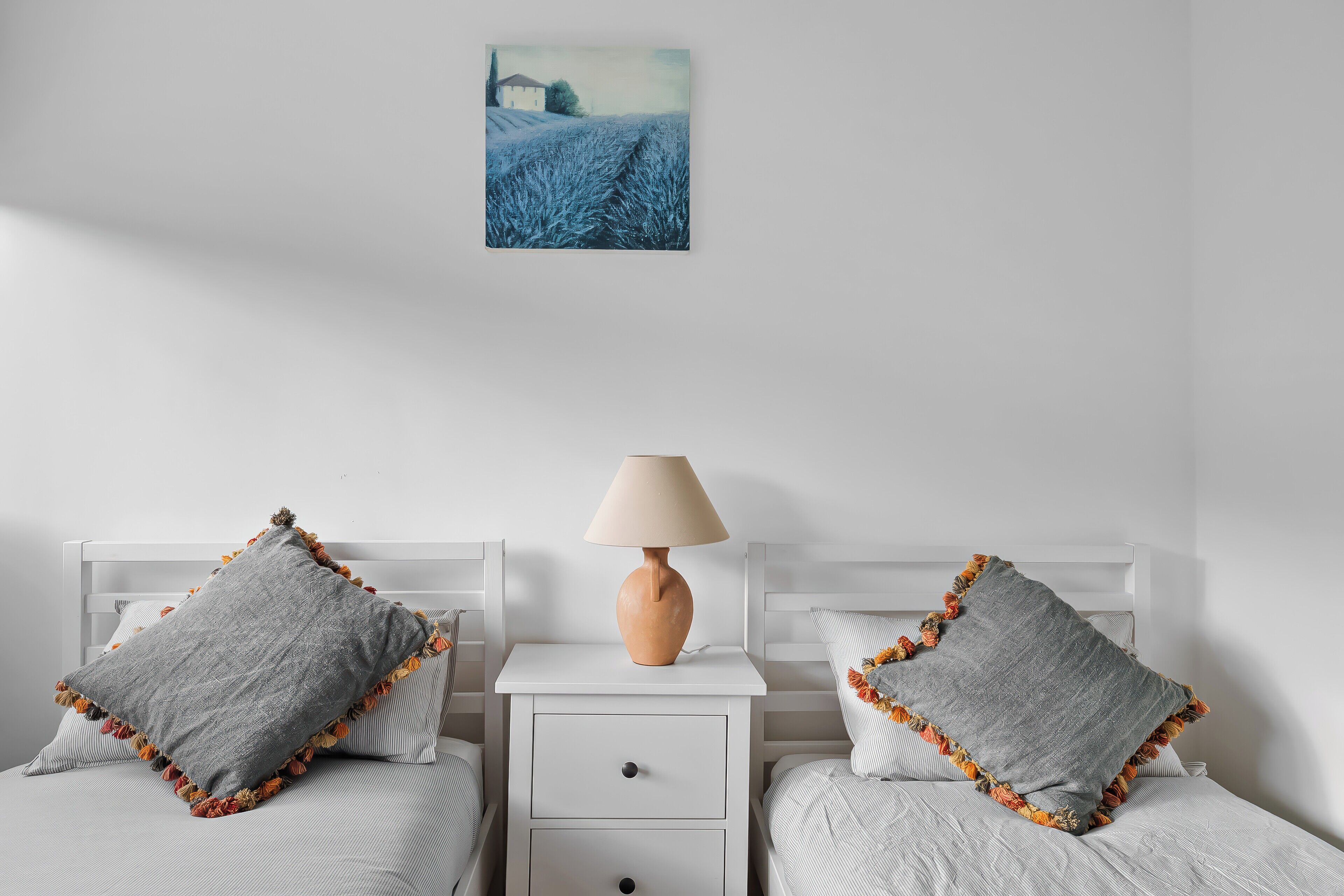 Un dormitorio con dos camas, una mesita de noche con lámpara y un cuadro en la pared.
