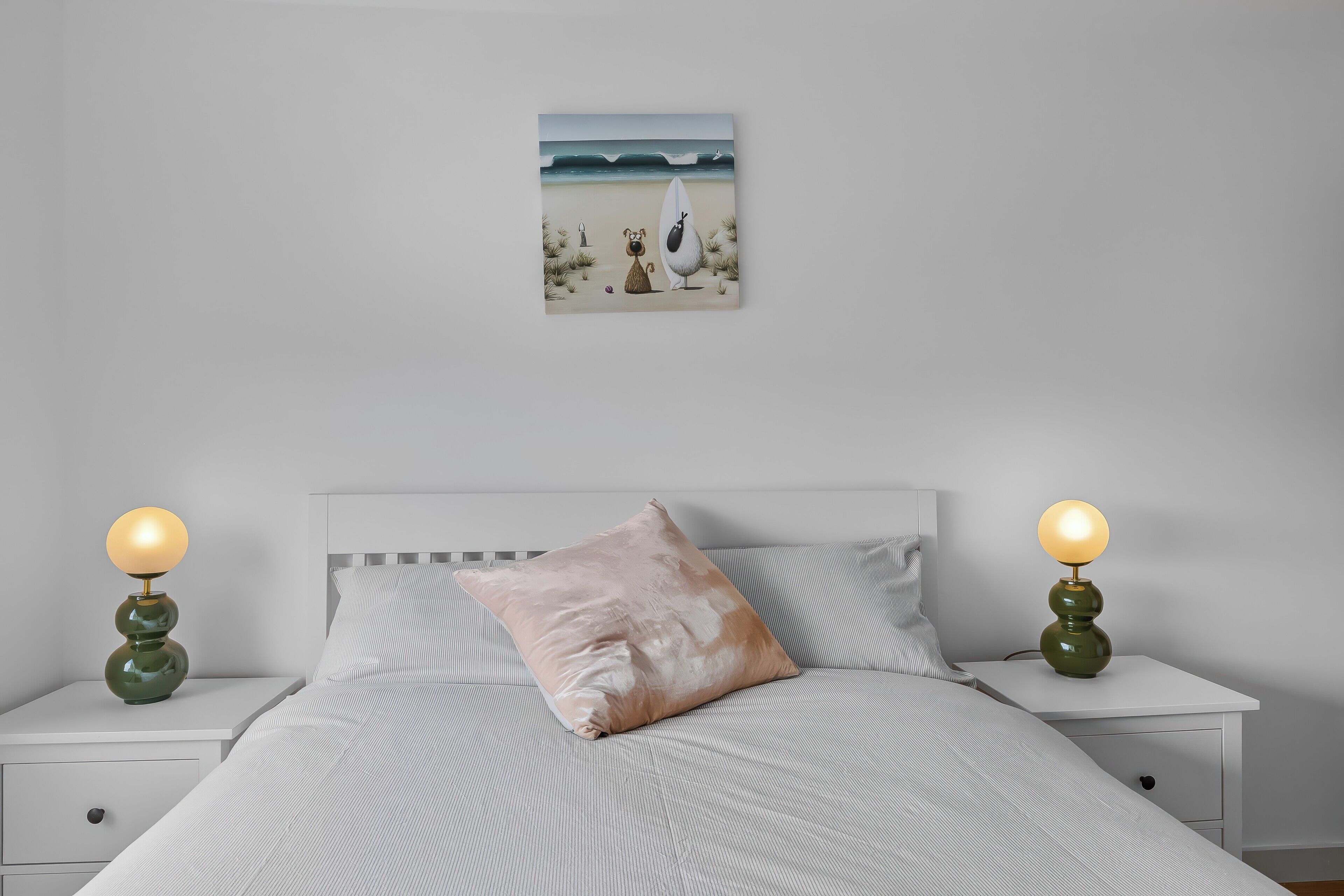 A bedroom with a bed, two bedside tables, a nightstand, a lamp, and a painting on the wall.