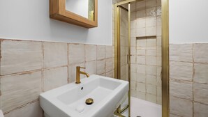 Ein Badezimmer mit einem weißen Waschbecken, einem spiegel mit Holzrahmen und einem Duschbereich mit goldener Umrandung.