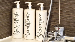 Drei weiße Flaschen mit den Aufschriften 'Baby Wash', 'Conditioner' und 'Shampoo' auf einem Badezimmerwaschbecken.