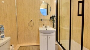 Ein modernes Badezimmer mit einer Glaskabine zur Dusche, einem weißen Waschbecken mit Spiegel darüber und einer Toilette mit Toilettenpapierhalter.