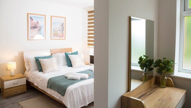A modern bedroom with a bed, bedside tables, a mirror, and framed pictures on the wall. - Manchester 2 Bedroom Apartment By Bevolve - Free Street Parking (Manchester)