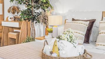 Een keurig opgemaakt slaapkamer met een bed, kussens, een nachtkastje, een lamp, een plantje en een mand met handdoeken.