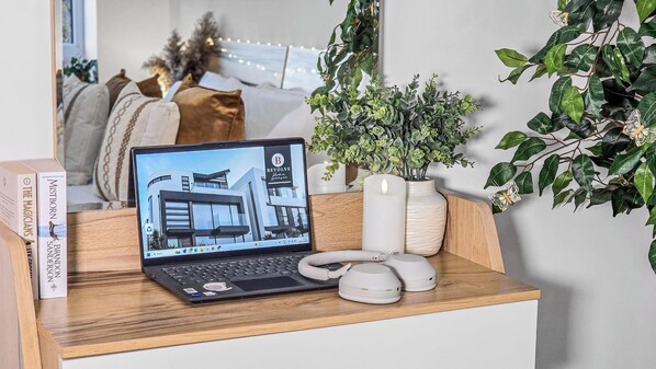 Una laptop sobre un escritorio de madera con una planta en maceta y dos dispositivos blancos, posiblemente parlantes, en frente.
