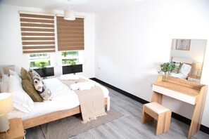 Een slaapkamer met een bed, nachtkastje, bankje, bureau en spiegel.