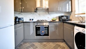 Cocina compacta con armarios grises, horno empotrado, microondas y lavadora.