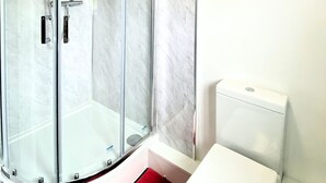 Un baño moderno con ducha envuelta en vidrio, inodoro blanco y paredes de mármol.