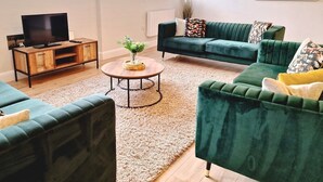 A modern living room with a green sofa, a wooden coffee table, and a TV on a wooden cabinet.
