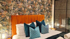 A neatly made bed with a patterned headboard, a bedside lamp, and a decorative wall with a tropical design.
