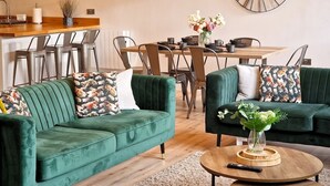 A living room with two green sofas, a wooden coffee table, and a dining area with a wooden table and chairs.
