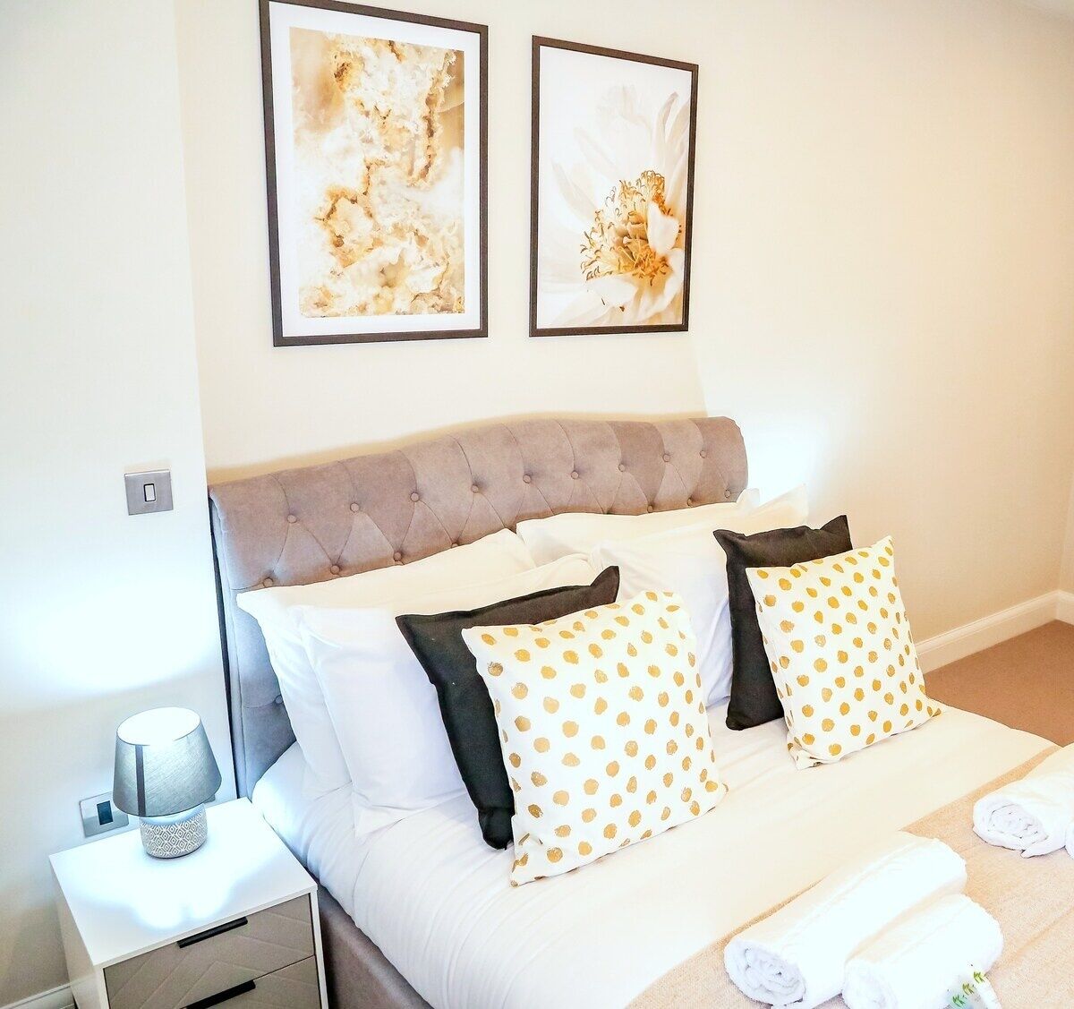 A neatly made bed with white and polka-dotted pillows, a tufted headboard, and a bedside table with a lamp.