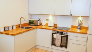 A modern kitchen with white cabinetry, a wooden countertop, a built-in oven, and a coffee maker. - Shrewsbury 1 Bedroom Flat By Bevolve (Shrewsbury)
