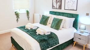 A neatly made bed with green and white bedding, a bedside table with a lamp, and framed pictures on the wall. - Shrewsbury 1 Bedroom Flat By Bevolve (Shrewsbury)