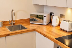 Une cuisine moderne équipée d’un évier en acier inoxydable, d’un four à micro-ondes Russell Hobbs blanc, d’une bouilloire et d’un grille-pain.