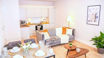 A modern living room with a dining area, a grey sofa, a coffee table, and a kitchen in the background.