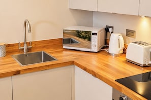 Una cocina moderna con un lavamanos de acero inoxidable, un microondas Russell Hobbs blanco, una tetera y un tostador.