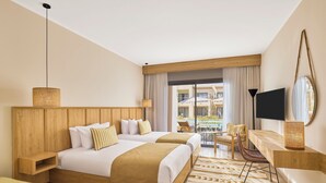 Habitación de hotel con dos camas, televisión, escritorio y vista al área de la piscina al aire libre.