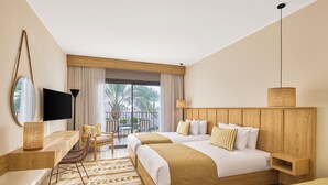 Habitación de hotel con dos camas, televisión, escritorio, silla, balcón con vistas y una lámpara colgante.
