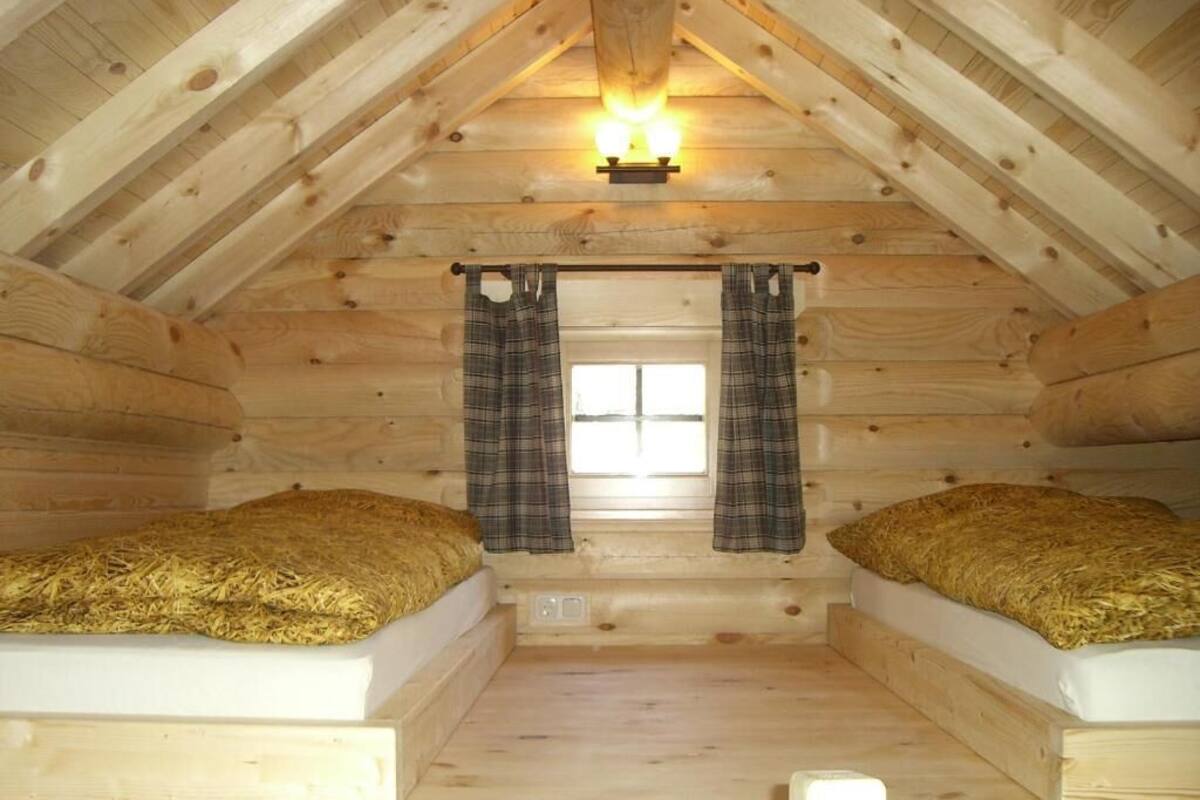 Een gezellig slaapkamer op zolder met twee stapelbedden, houten wanden, een schuine balkenlaag en een raam met ruitjesgordijnen.