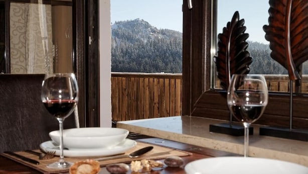 A dining table set with white plates, two wine glasses, and a wooden leaf decoration. - Montara Suites Bodenmais (Bodenmais)