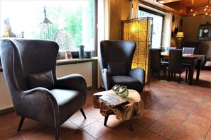 Een knus ingerichte kamer met twee leren fauteuils, een houten salontafel en een eethoek met tafel en stoelen.