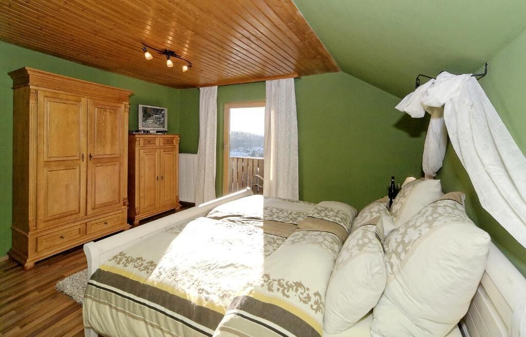 A bedroom with a wooden wardrobe, a bed with white bedding, and a view of a snowy landscape through a window.